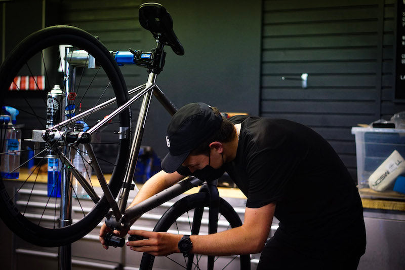 Someone fixing a bike on a stand with a black wall in the background and other accessories